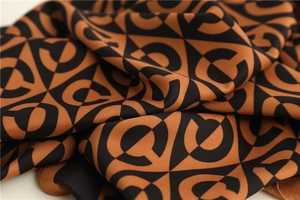 Detailed close-up of smooth satin silk scarf with brown and black geometric C pattern