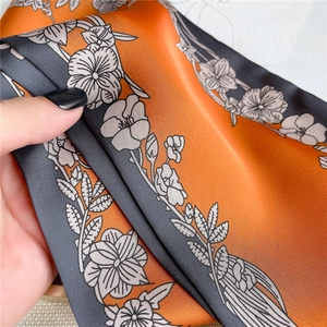 Detail view of orange and grey floral scarf showing smooth silk texture and drape