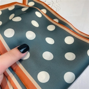 Close-up of retro dark green polka dot silk scarf with orange striped border details