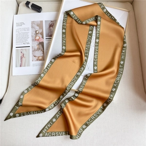 Detail of a luxury golden silk twilly scarf with floral prints and green borders