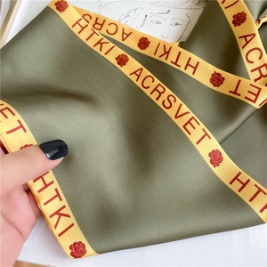 Detail of silk scarf showing rose pattern, green satin texture, and yellow contrast edges