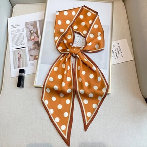 Close-up of orange silk twilly scarf with white polka dots on a stylish magazine layout