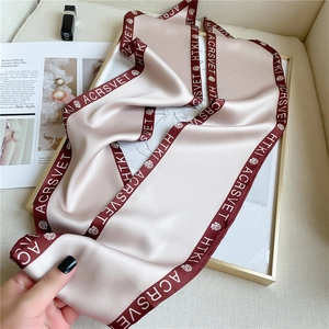 Close-up of champagne silk scarf with rose patterns and dark red borders on artistic base