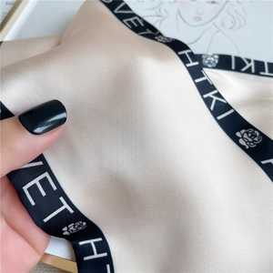 Macro detail of silk-like champagne gold scarf with black letter print and floral pattern