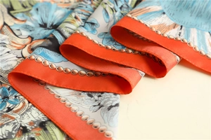 Detail of silk scarf with orange hem, golden chain patterns and floral prints