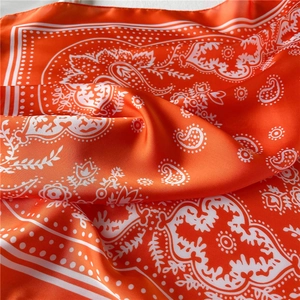 Close-up of vibrant orange paisley silk-like scarf with intricate floral patterns