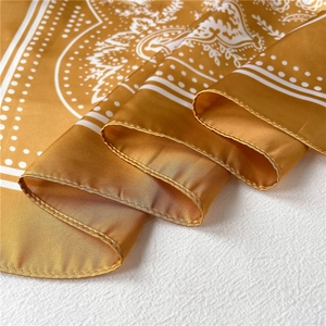Macro view of paisley patterns and fine rolled edges on a silky yellow square scarf