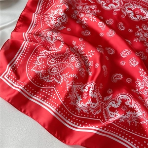 Close-up of red silk-like square scarf with white paisley pattern and smooth texture
