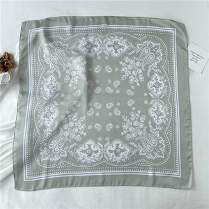 Flat lay of a grey-green paisley square scarf on white linen with dried flowers