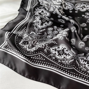 Detailed macro view of black silk-like scarf featuring white paisley pattern and smooth texture