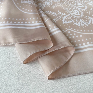 Macro detail of silk-feel champagne scarf featuring elegant paisley patterns and hemmed edges