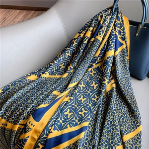 Detail of silk-like long shawl with classic H-pattern and chain floral print on gray sofa