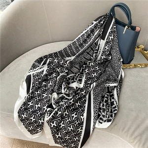 Elegant black and white printed scarf with geometric H patterns draped on a handbag