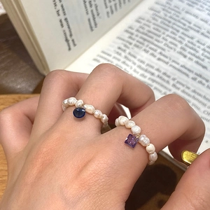 Macro shot of freshwater pearl rings with blue and purple gemstone charms on model hand