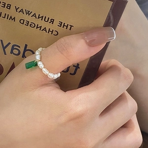 Detailed shot of elastic pearl ring with emerald green zircon pendant on model hand