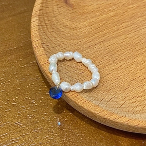 Detail of freshwater pearl beaded ring featuring a blue gemstone pendant on a wooden tray