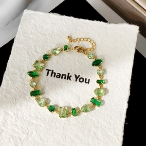 Detailed macro view of gold bracelet featuring multi-shape green zircon gemstones and lobster clasp
