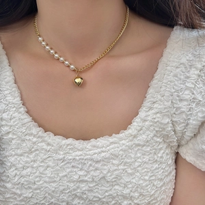 Detail of a pearl and gold chain necklace featuring a polished gold heart pendant