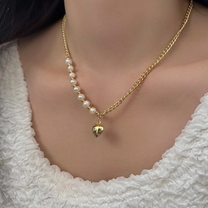 Detail of a pearl and gold chain heart pendant necklace worn on an elegant female neck
