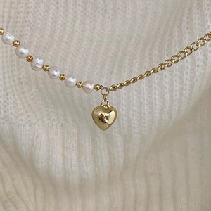 Detail of pearl and gold chain necklace with a heart pendant on a white sweater
