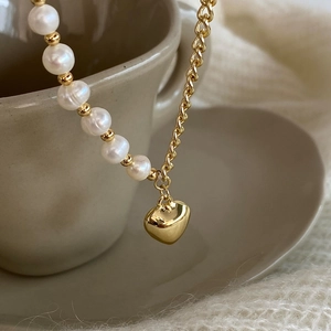 French style pearl and gold chain necklace with heart pendant on a ceramic cup