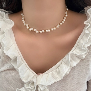 Detailed view of pearl necklace with gold beads on model wearing white lace top