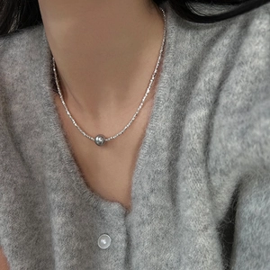 Détail du collier à perles argentées avec un grand pendentif boule en métal sur tricot