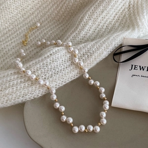 Detailed shot of a pearl necklace with gold beads on a white knit sweater background