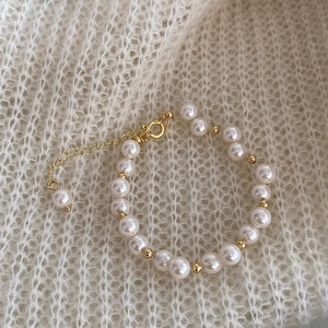 Detail of elegant pearl bracelet with gold spherical beads on white knit texture