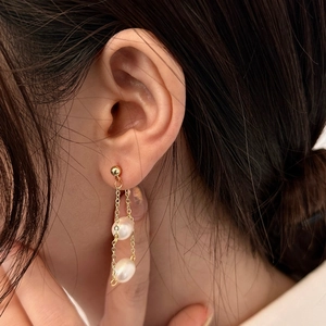 Close-up of gold chain earrings with baroque freshwater pearls worn by a model