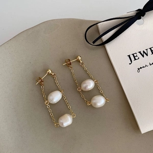 Close-up of gold chain tassel earrings with freshwater pearls on a ceramic plate