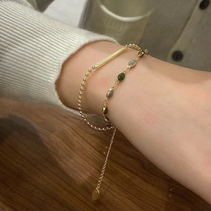 Double-layered gold chain bracelet with olive green beads and metal bar on wrist