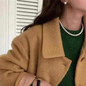 Close-up of elegant pearl necklace and matching earrings paired with an autumn wool coat