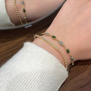 Close-up of double-layer vintage gold bracelet with green and grey gemstones on wrist