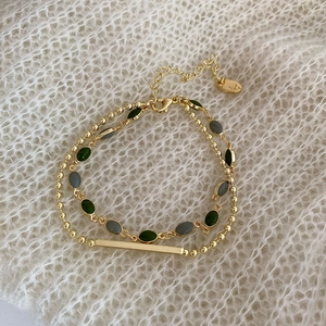 Detail of double-layer vintage bracelet with emerald beads on a white knit background
