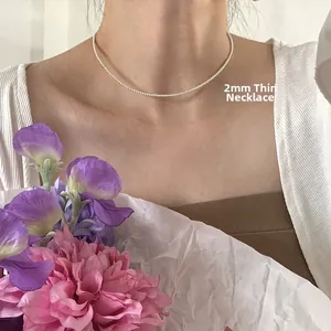 Macro detail of a 2mm ultra-fine silver pearl necklace worn by a model with flowers