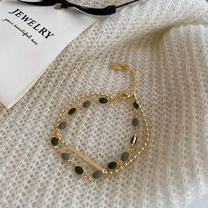 Detail of a double-layered gold chain bracelet with green and grey oval enamel beads