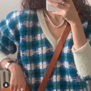 Detail of a blue and green plaid knit sweater with white ribbed cuffs and pearl necklace