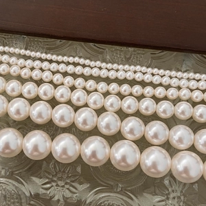 Macro shot showing five sizes of round ivory pearls with elegant luster on textured glass