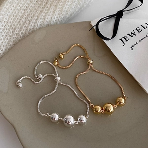 Detail of adjustable gold and silver bead bracelets on a ceramic tray with a gift bag