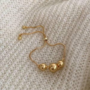 Detailed view of adjustable gold slider bracelet with three polished beads on soft knit