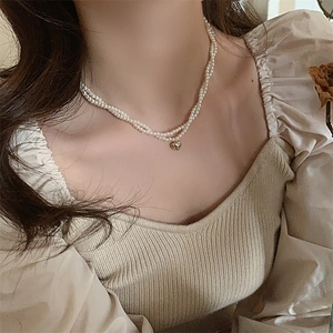 Dettaglio di una collana di perle a doppio strato con ciondolo a cuore dorato su modella