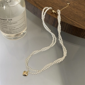 Dettaglio della collana di perle a doppio strato con ciondolo a cuore dorato e chiusura a moschettone