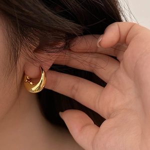 Dettaglio dell'orecchino ovale in oro lucido indossato da una modella con stile