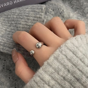 Detail of silver crossover open ring with spherical tips worn over a grey knit sweater