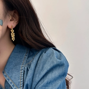 Macro detail of elegant golden beaded cluster earrings worn with a denim jacket