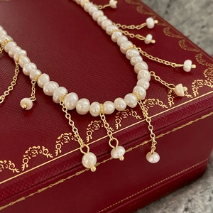 Vue détaillée des perles d'eau douce avec chaîne à pompons dorée sur un écrin à bijoux rouge