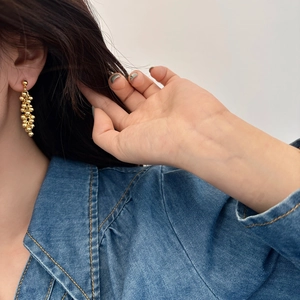 Fashionable gold beaded grape cluster tassel earrings worn by a model in natural light