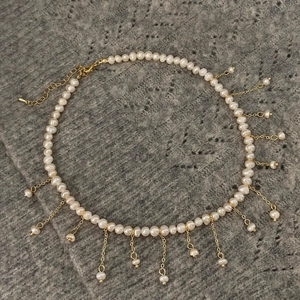 Détail d'un collier à pampilles en perles d'eau douce avec chaînes dorées sur fond sombre