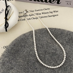 Gros plan d'un collier de perles blanches avec fermoir argenté sur tissu texturé